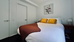A bedroom with a bed, a nightstand, a lamp, and a painting on the wall. - Queenstown City •Walk to Town •Free Parking •A/C •Balcony •Mountain Views (Queenstown)