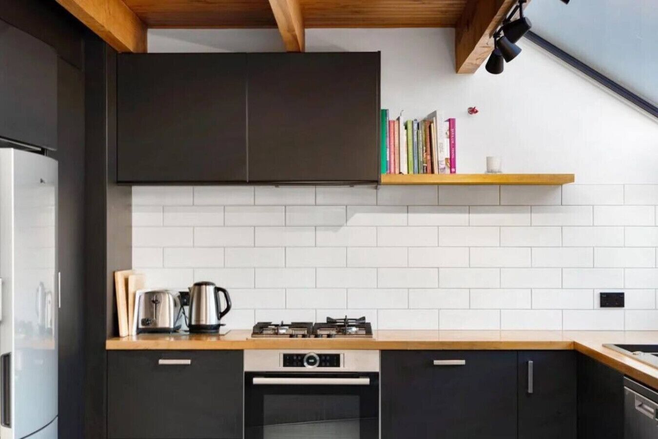 A modern kitchen with dark cabinets, a gas stove, a coffee maker, and a bookshelf above the counter.
