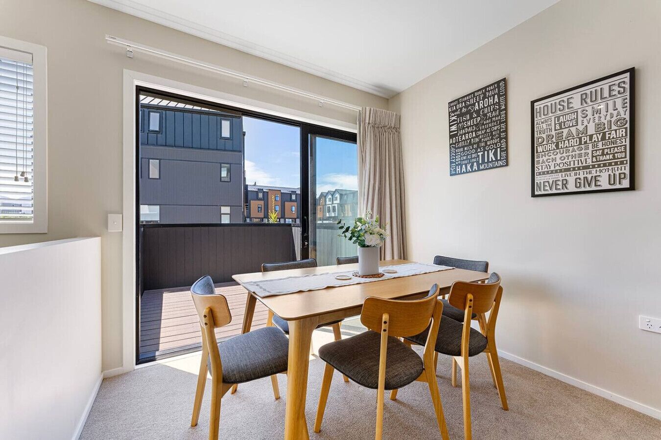 A modern dining area with a table and chairs, a view through a glass door to the outside, and motivational wall art.