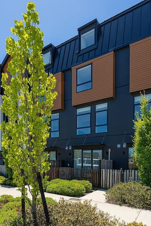 Un bâtiment moderne à plusieurs étages, doté de grandes fenêtres, d’un toit plat et d’une clôture en bois qui entoure la propriété.