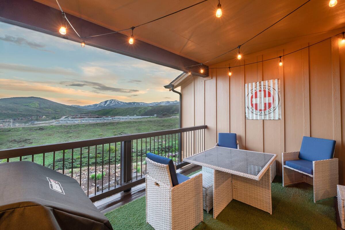 A balcony with wicker furniture, a table, and a view of a mountainous landscape.