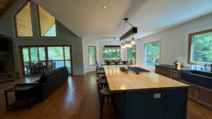 A spacious kitchen with a large island, wooden flooring, and large windows offering views of the outdoors. - New Riverfront Retreat – Ultimate Privacy, Stunning Views, & Dog-friendly! (Bryson City)