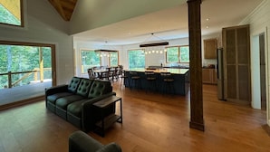 A spacious living area with a large sofa, a dining table, and a kitchen with a bar. - New Riverfront Retreat – Ultimate Privacy, Stunning Views, & Dog-friendly! (Bryson City)