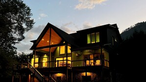 A multi-story house with a prominent balcony and a stone fireplace. - New Riverfront Retreat – Ultimate Privacy, Stunning Views, & Dog-friendly! (Bryson City)