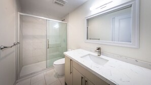 Une salle de bain moderne avec une douche Ă parois de verre, des toilettes blanches et un lavabo en marbre.