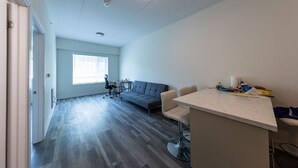 Une pièce moderne et bien éclairée, avec un canapé gris, une petite table à manger et un coin bar.