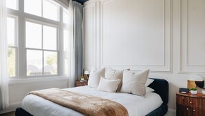 Un dormitorio ordenado con una cama grande, una ventana con cortinas y una mesita de noche con lámpara.