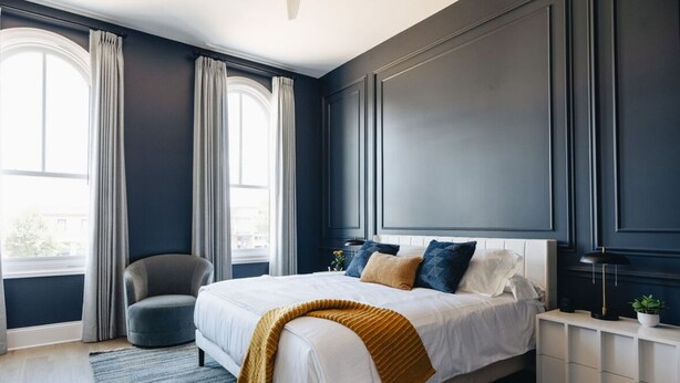Un dormitorio moderno con una cama grande, una silla y una mesita de noche con una lámpara y una planta.