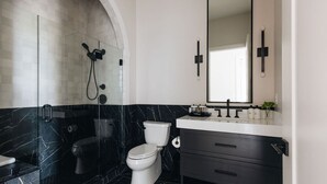 Un baño moderno con ducha cubierta de vidrio, inodoro blanco y piso de mármol negro.