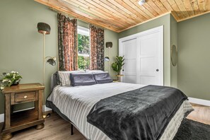 A bedroom with a bed, a nightstand, a lamp, and a door. - Cozy, stylish, and surrounded by nature; Sojourn Hideaway is the perfect getaway (Windsor)