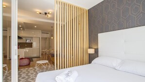 A hotel room with a large bed, a wooden partition, a patterned wall, and a view of the kitchen and dining area.