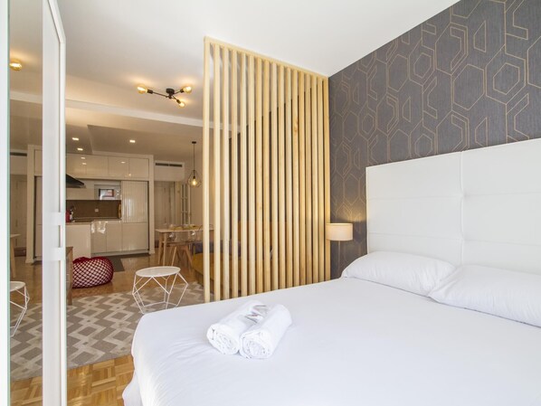 Une chambre d’hôtel avec un grand lit, une cloison en bois, un mur à motifs et une vue sur la cuisine et l’espace repas.