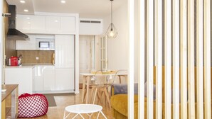 A modern kitchen with white cabinets, a microwave, and a red coffee machine. There is a dining area with a yellow sofa and a white table.