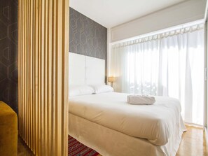 Una camera d'albergo con un letto grande, un comodino, una lampada e una finestra con tende.