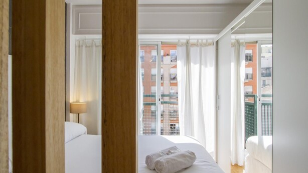 A hotel room with a bed, a window with curtains, and a view of a building outside.