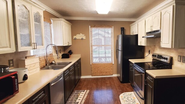 A kitchen with white cabinets, a black refrigerator, a stove, and a sink.
