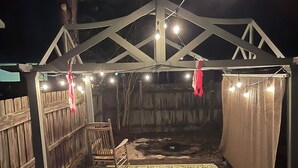 A covered outdoor area with a wooden deck, a metal barrel, and string lights.