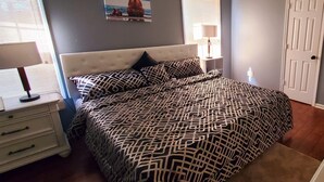 A bedroom with a tufted headboard, patterned bedding, a nightstand with a lamp, and a door.