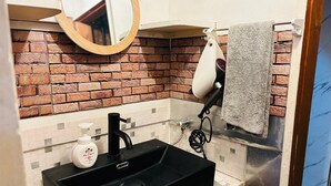 Et badeværelse med en sort vask, et spejl, et håndklædestativ og en backsplash af mursten.