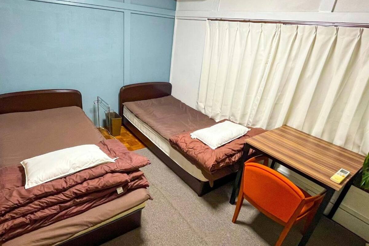 A small room with two single beds, a wooden table, and an orange chair.