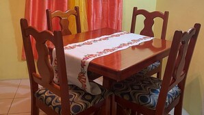 A dining area with a wooden table and chairs, a floral tablecloth, and a curtain with red and yellow panels. - Charming 2 bedroom house with AC, WIFI  (Jimmit mahaut)