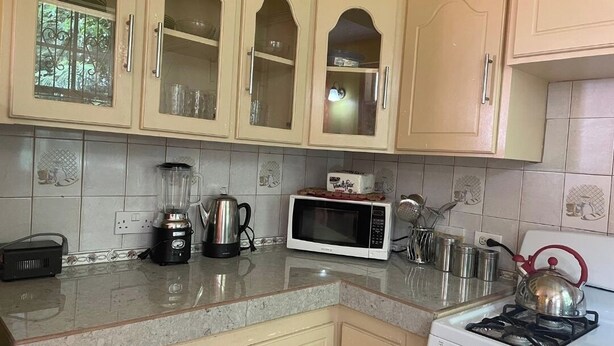 A kitchen with beige cabinets, a microwave, a kettle, and a gas stove. - Charming 2 bedroom house with AC, WIFI  (Jimmit mahaut)
