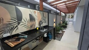 A modern kitchen with a black countertop, stainless steel sink, and a wooden cutting board. - Sunset House (Chácaras Mogiano Bertioga)