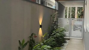 A covered walkway with a wooden ceiling, a wall with a light fixture, and a gate. - Sunset House (Chácaras Mogiano Bertioga)
