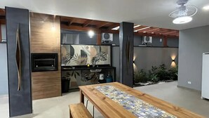 A modern kitchen with a built-in oven, a wooden dining table with a patterned table runner, and a bench. - Sunset House (Chácaras Mogiano Bertioga)