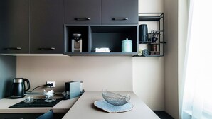 Una cuina moderna amb armaris foscos, una màquina de cafè, una tetera i una estantalla amb objectes de cuina.
