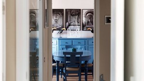 Passadís que condueix a una cuina blava amb una taula rodona i cadires, i vista a un corredor amb arcs.