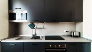 Una cuina moderna amb armaris foscos, un forn d'acer inoxidable, un microones integrat, un rentaplat i una torradora.