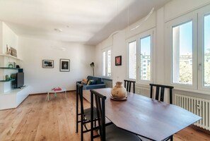 A modern living space with a dining table, chairs, a sofa, and a TV.