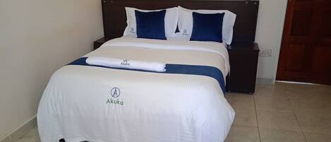 A neatly made bed with a white and blue bedspread, a matching pillow, and a white towel on the bed.