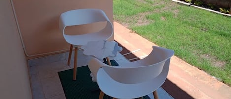 Two white chairs with wooden legs on a green mat outside a building with a tiled floor.
