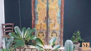 Uma porta de madeira com figuras pintadas, uma cadeira e vasos com plantas.