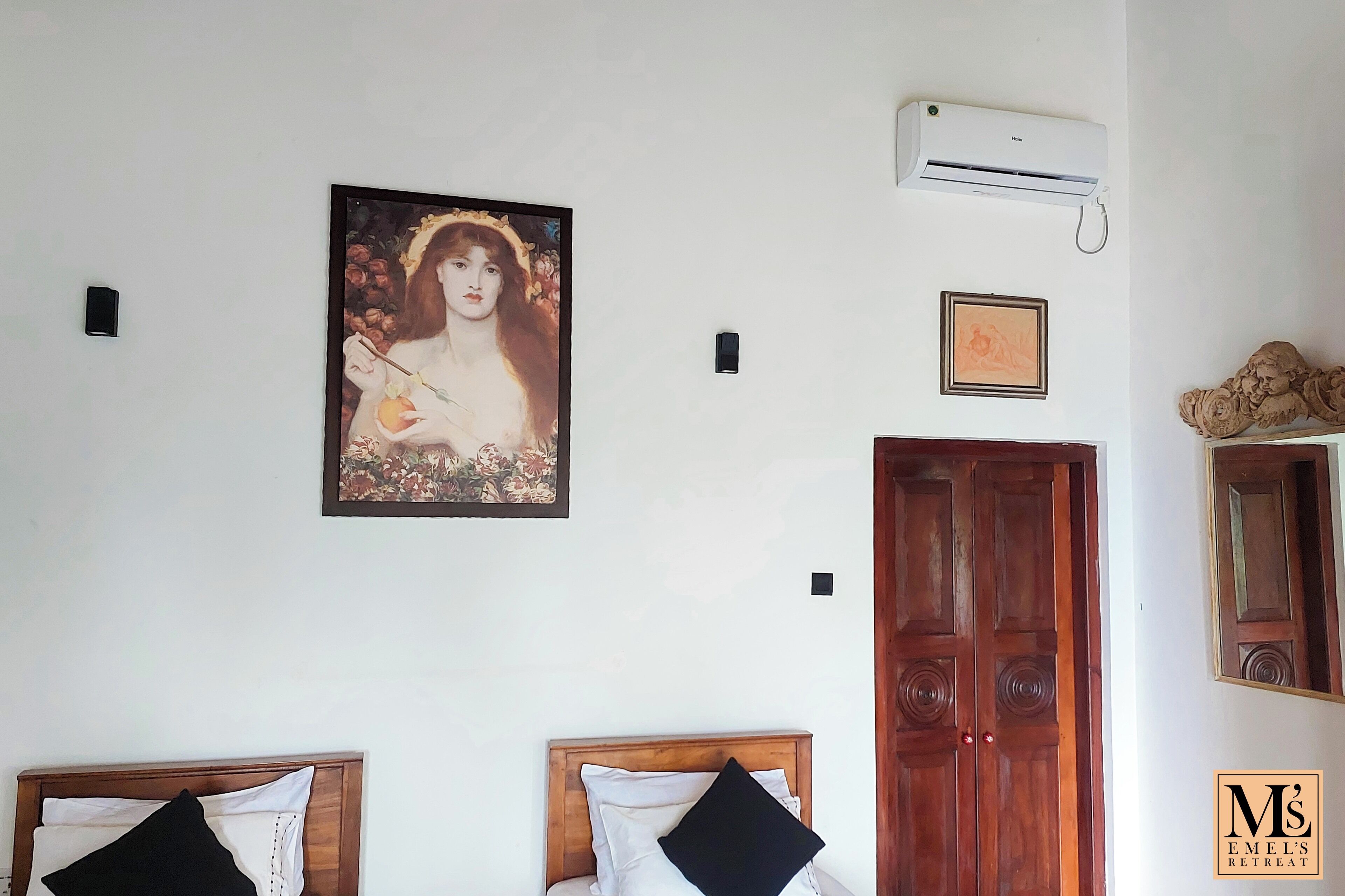 A bedroom with two beds, a wooden door, an air conditioning unit, and a framed artwork on the wall.