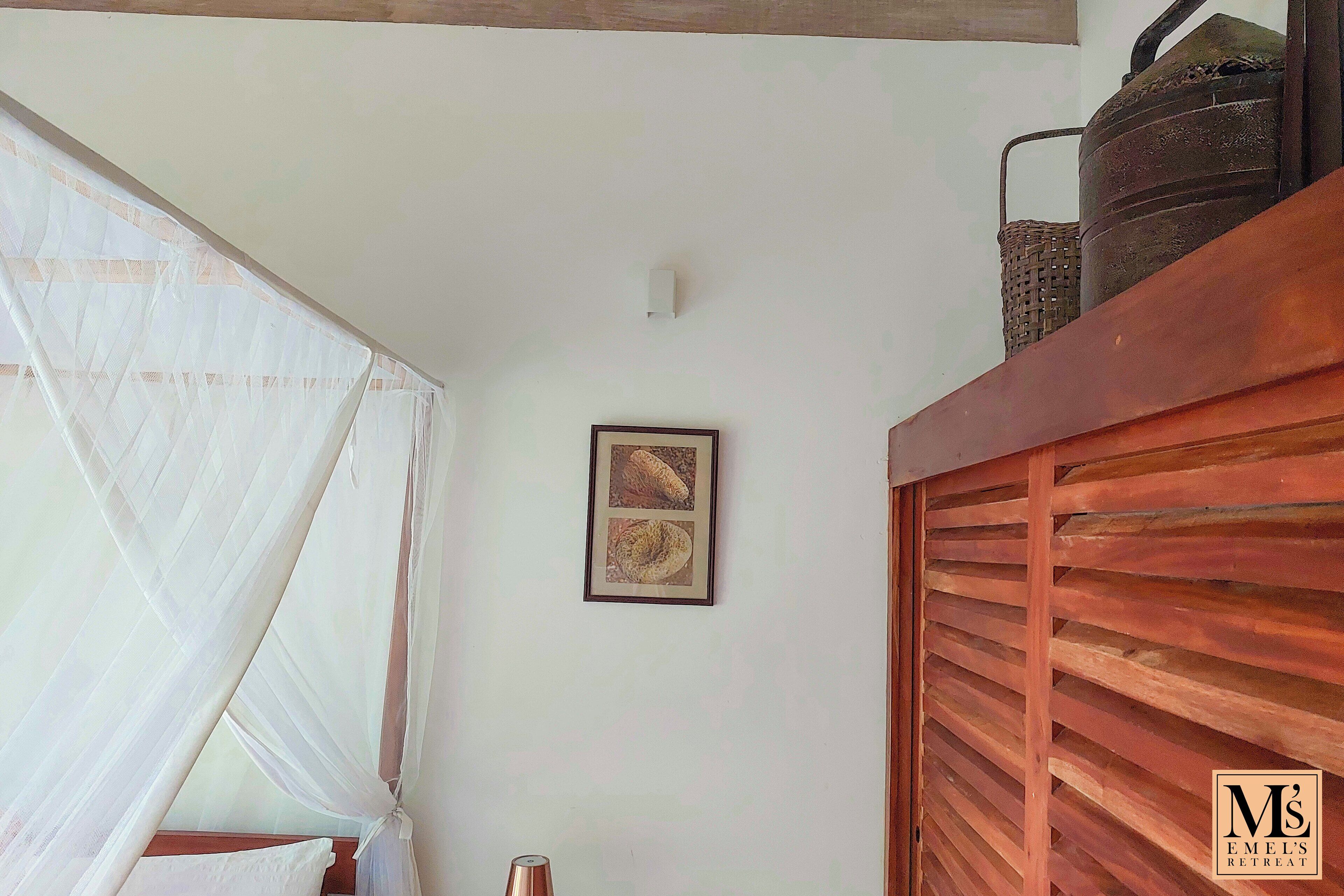 A room with a bed, a wall-mounted picture, a ceiling light, and a wooden slatted partition.