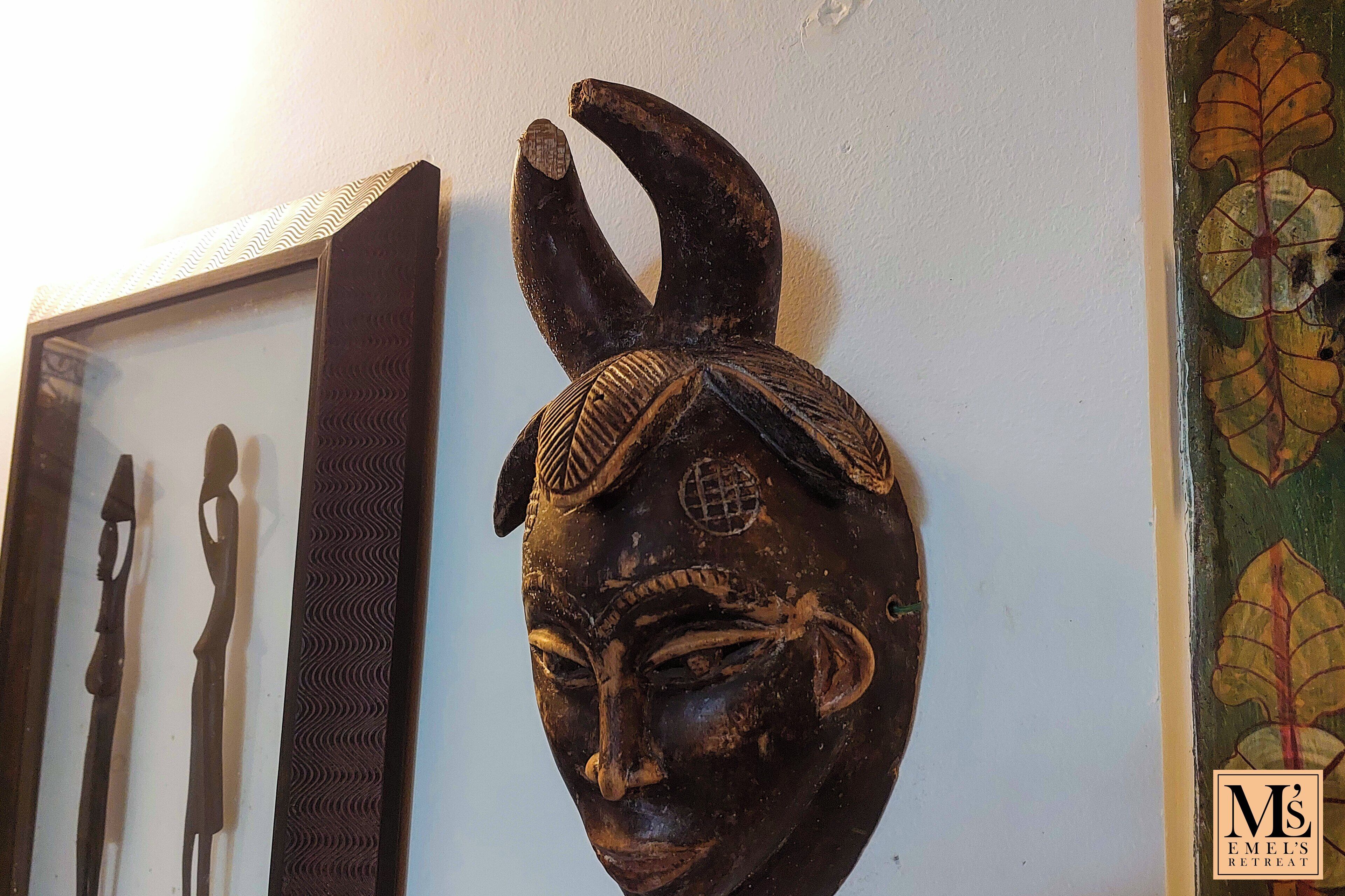 Una pared con una escultura enmarcada y una cabeza de madera tallada.