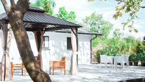 A covered outdoor seating area with wooden chairs and a table, surrounded by potted plants and trees. - Casita Canal  (Naples)