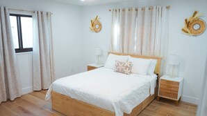 A bedroom with a wooden bed, white bedding, two bedside tables with lamps, and a window with curtains. - Casita Canal  (Naples)