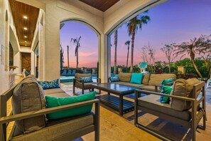 An outdoor seating area with sofas and tables, a pool, and palm trees.