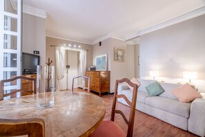 Una sala de estar con una mesa redonda de madera, un sofá, un televisor y un mueble.