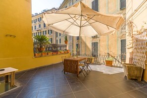 Ein Balkon mit Tisch und Stühlen, einem großen Sonnenschirm, Topfpflanzen und Blick auf Gebäude.