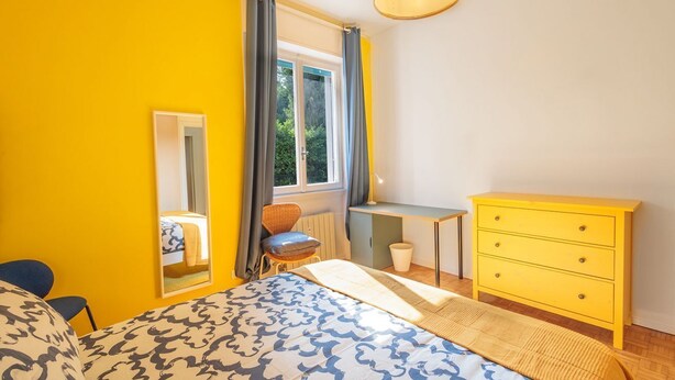 Une chambre à coucher comprenant un lit, un bureau, une chaise, une commode, un miroir et une fenêtre avec des rideaux.