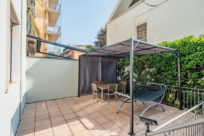 Een overdekt terras met een tafel, stoelen, een hangmat en een metalen hekwerk.