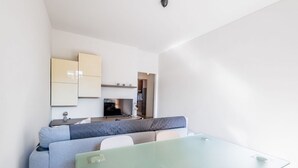 Un salon moderne et minimaliste, avec une table à manger en verre, un canapé gris et un coin cuisine en arrière-plan.