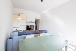 Un salon moderne et minimaliste, avec une table à manger en verre, un canapé gris et un coin cuisine en arrière-plan.