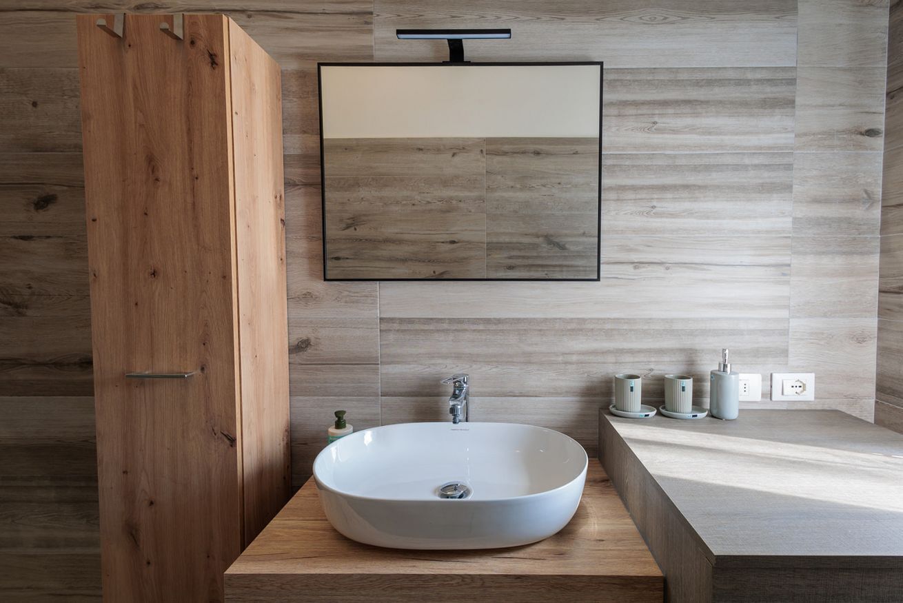 A modern bathroom with a wooden vanity, a white sink, and a mirror.