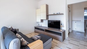 Un salon moderne avec un canapé, un téléviseur, des étagères intégrées et une vue sur l’extérieur.